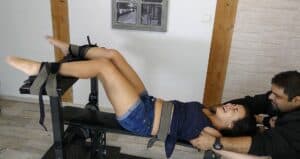 Woman restrained on foot tickling device, smiling and laughing during tickling session.